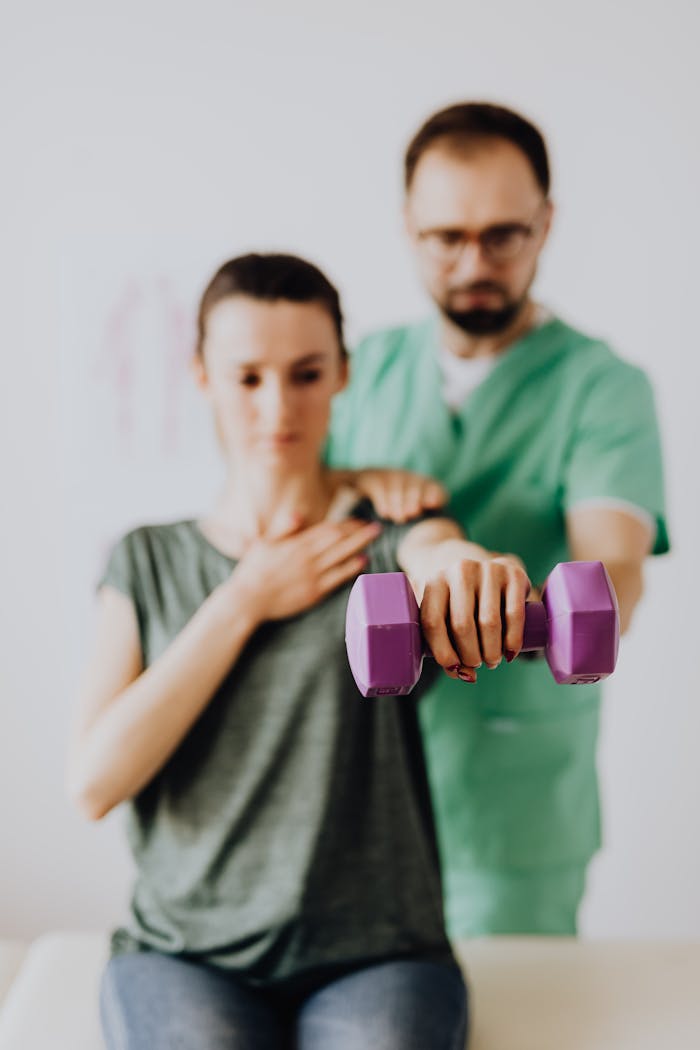 A therapist assists a patient with dumbbell exercises in a clinic setting.